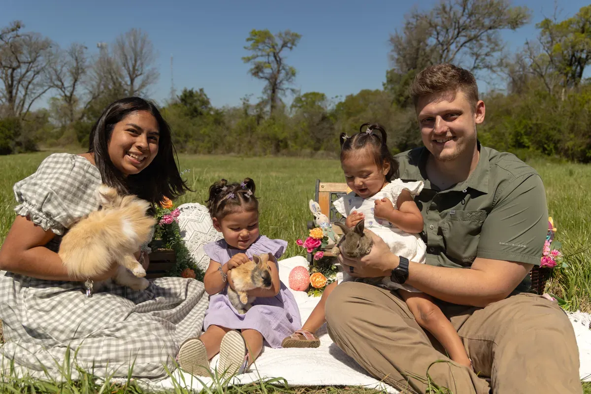 Nic, his spouse, two daughters, and their dog sitting together on a blanket in a sunny field